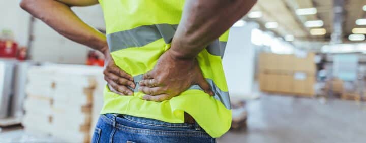 Ansatt som har vondt i ryggen ved en arbeidsstasjon i produksjonslokale
